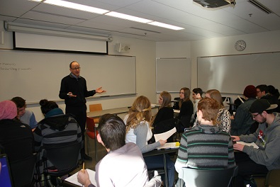 An instructor talks to a group of First Year students in front of a whiteboard in a classroom.